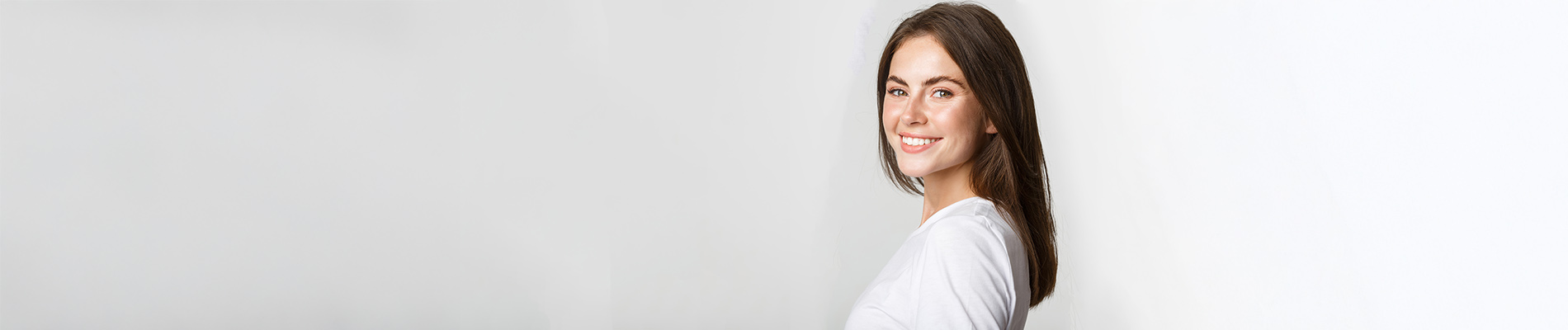The image is a photograph of a woman with light skin, smiling at the camera. She appears to be in her late twenties or early thirties and has long hair. Her eyes are looking directly at the camera, and she is holding up her index finger near her mouth as if she s making a point or emphasizing something. The background is plain and light-colored, which suggests that this could be a stock photo used for various purposes such as advertising, personal branding, or lifestyle content.