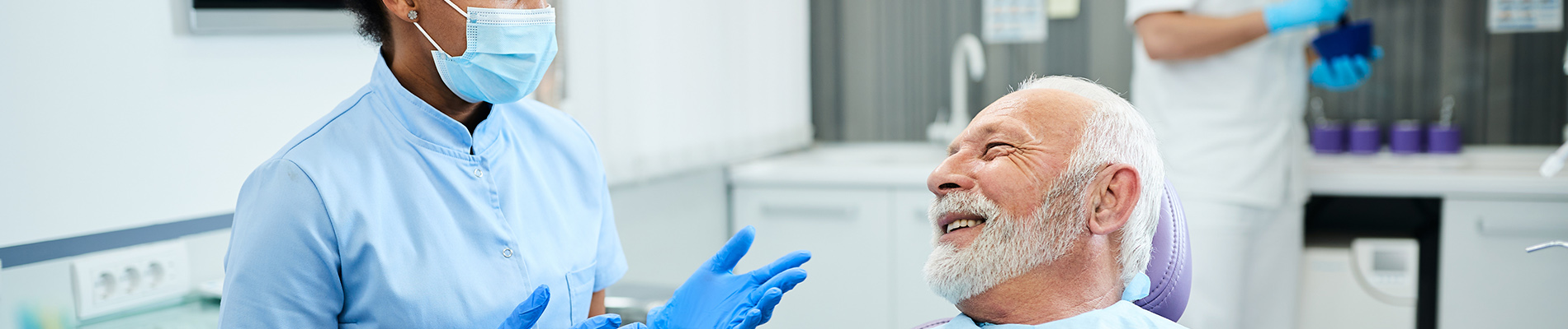 A person is seated in a dental chair, receiving care from a dental professional who stands behind them.